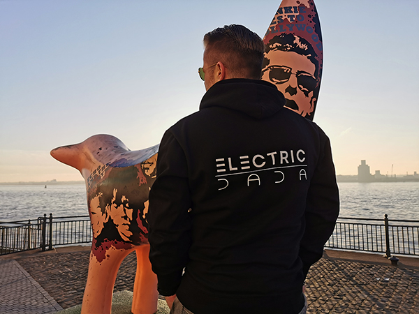 You can see Micha Schrodt aka Jan de Vice from Electric Dada, standing at the Queens Docks in Liverpool (England). He is wearing a black Electric Dada hoodie with the Electric Dada logo printed in white on the back!  